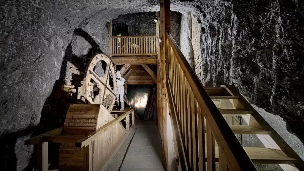 The oldest salt mine in Poland is found in Bochnia. This picture portrays a wooden staircase and an exhibition of a statue using old salt mining machinery. 
